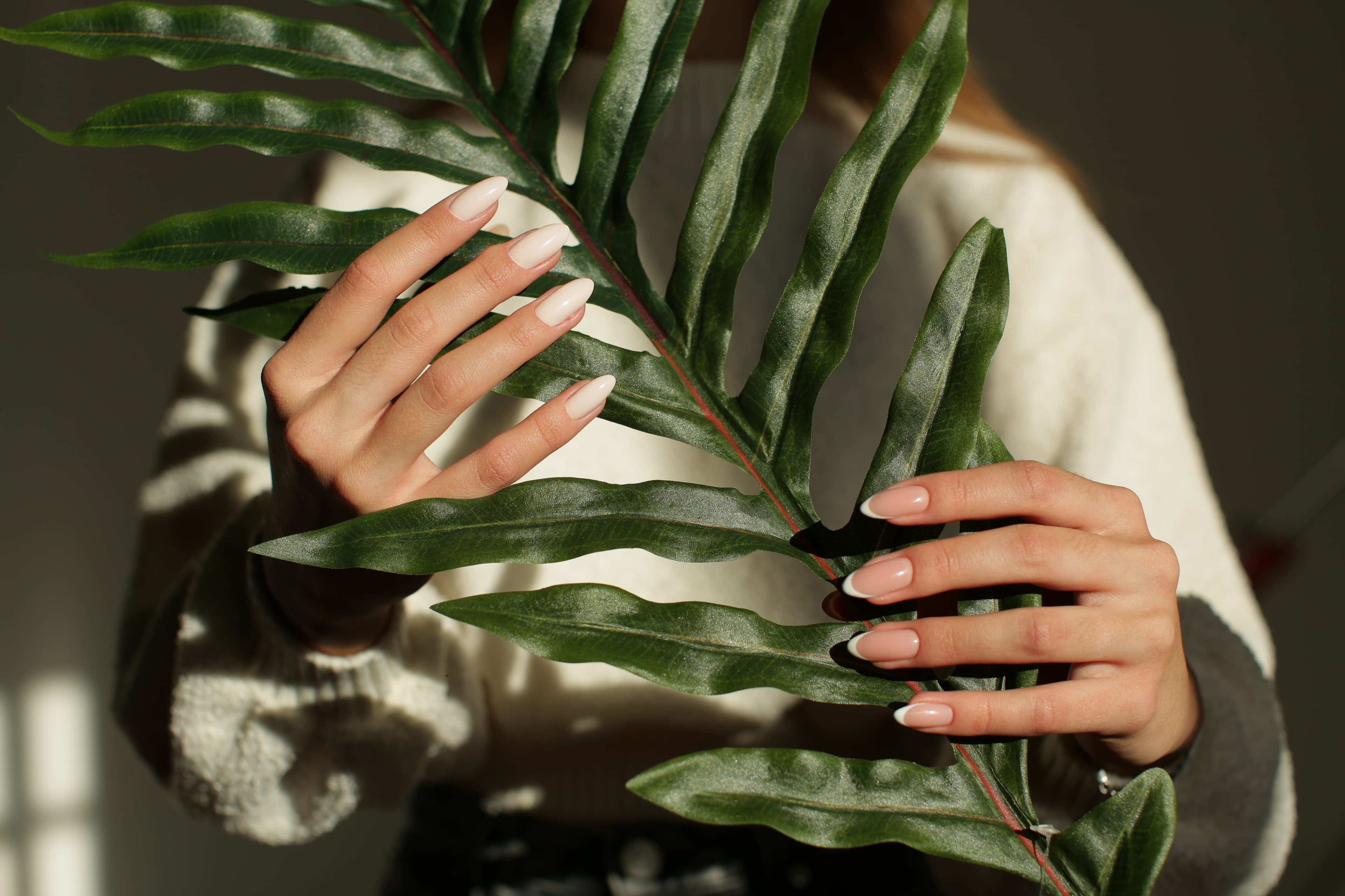 Client admiring her freshly finished nude manicure beside lush greenery